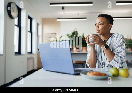 Une jeune femme d'affaires attentionnés qui boit du café sur un ordinateur portable au bureau Banque D'Images