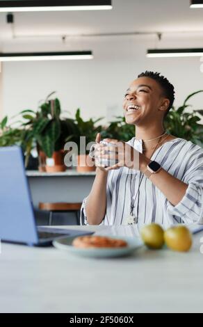 Bonne femme d'affaires avec un café qui rit sur un ordinateur portable au bureau Banque D'Images