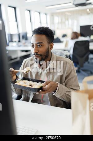 Homme d'affaires qui mange des sushis à emporter à l'ordinateur au bureau Banque D'Images