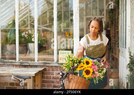 Fleuriste femme plaçant des fleurs dans un panier à vélos à l'extérieur du magasin Banque D'Images