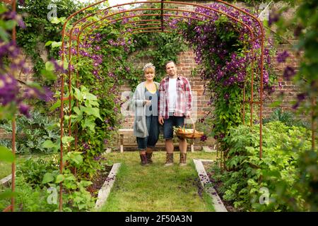 Portrait couple heureux récolte des légumes sous le treillis de fleurs Banque D'Images