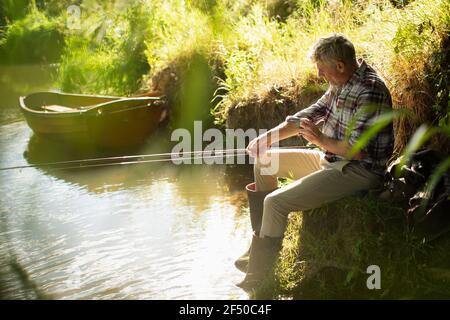 Homme pêche à la mouche sur les manches au bord de la rivière ensoleillée Banque D'Images