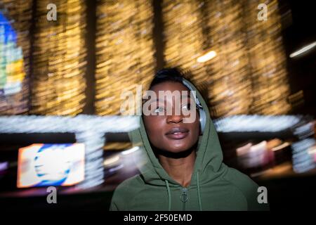 Jeune femme à capuche et écouteurs sous les lumières de la ville Banque D'Images