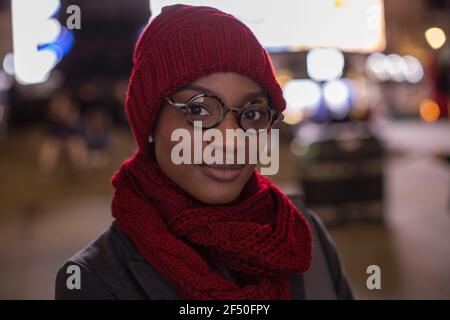 Portrait confiante jeune femme en foulard de lunettes et chapeau à nuit Banque D'Images