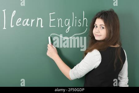 Un jeune pré-adolescent souriant écrit dans la craie « J'apprends l'anglais » sur fond vert. Banque D'Images