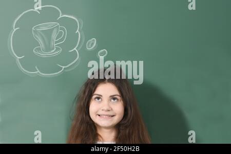 Un jeune pré-adolescent souriant rêve d'une tasse de thé sur fond vert de la commission scolaire. Banque D'Images