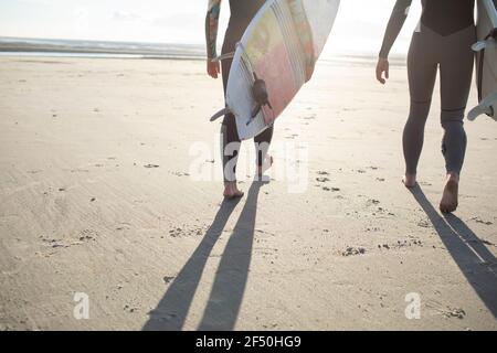 Des surfeurs féminins portant des planches de surf sur une plage de sable ensoleillé Banque D'Images