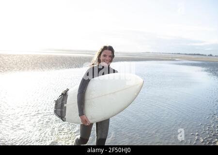 Portrait bonne jeune femme surfeuse avec planche de surf dans l'océan ensoleillé surf Banque D'Images