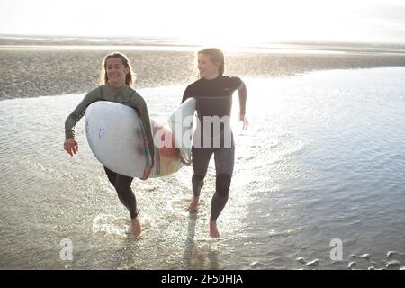 Jeunes femmes surfeurs heureux courant avec des planches de surf dans l'océan ensoleillé surf Banque D'Images