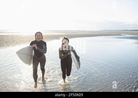 Jeunes femmes surfeurs insouciantes courant avec des planches de surf dans l'océan ensoleillé Banque D'Images