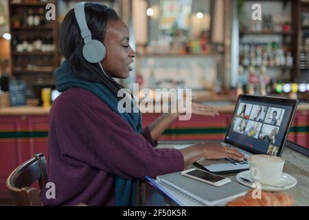 Jeune femme avec casque, chat vidéo avec des collègues dans un café Banque D'Images