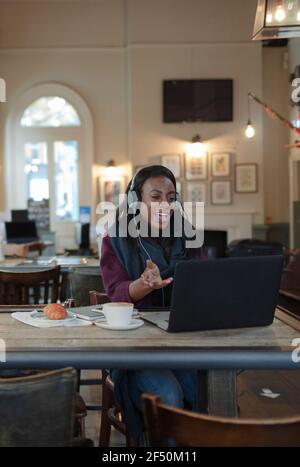 Femme d'affaires avec casque vidéo conférence à l'ordinateur portable dans le café Banque D'Images