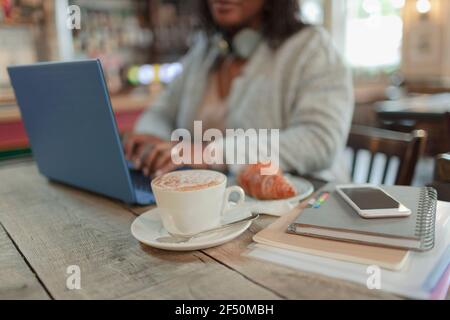 Femme travaillant sur un ordinateur portable à côté d'un croissant et d'un cappuccino café Banque D'Images