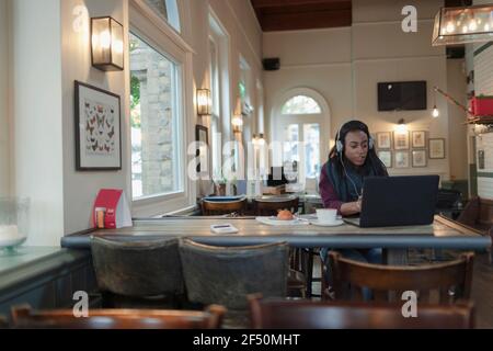 Femme d'affaires avec casque travaillant à l'ordinateur portable dans le café Banque D'Images