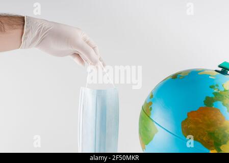 vue rognée de l'homme en latex gant tenant le masque médical près du globe isolé sur gris, concept écologique Banque D'Images