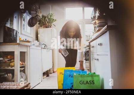 Femme triant le recyclage dans des sacs sur le plancher de la cuisine Banque D'Images