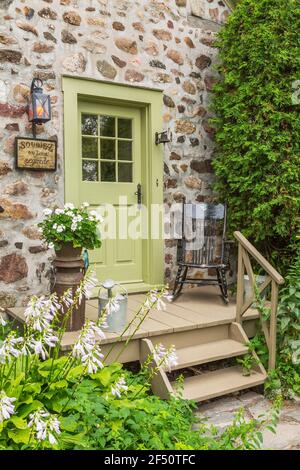 Ancienne maison en pierre de champ Canadiana vers 1735 avec porte latérale vert lime entrée et porche en bois clair décodé avec un bois noir fauteuil à bascule ancien Banque D'Images