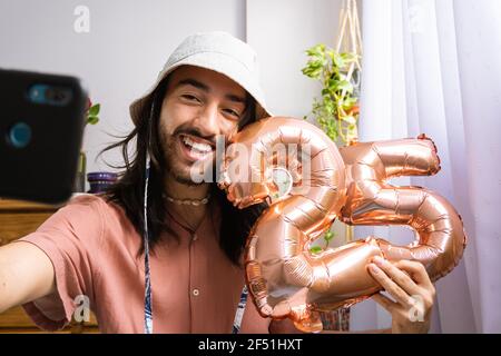 Jeune styliste attrayant prenant seul un selfie, tenant un ballon d'air métallique, célébrant son 25ème anniversaire. Ballon métallique avec le numéro 25. Banque D'Images