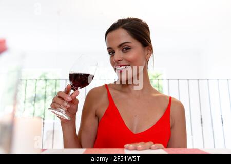 Femme caucasienne assise sur le bureau ayant une vidéo chat boire vin et sourire Banque D'Images