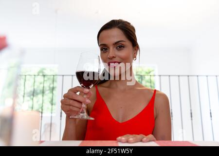 Femme caucasienne assise sur le bureau ayant une vidéo chat boire vin et sourire Banque D'Images