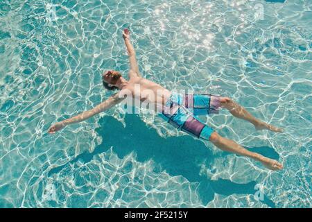 Homme flottant sur l'eau bleue en tirant avec les bras étirés large sous la lumière directe du soleil Banque D'Images