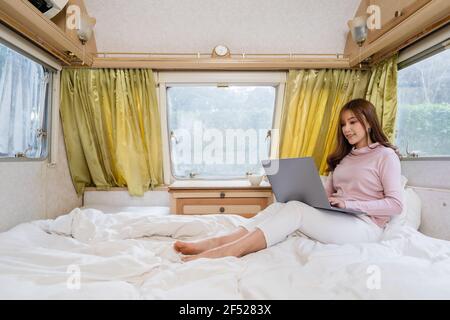 jeune femme utilisant un ordinateur portable sur le lit d'un campeur Camping camping-car Banque D'Images