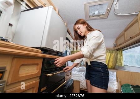 Une jeune femme cuisine dans la cuisine d'une camionnette de camping-car autocaravane Banque D'Images