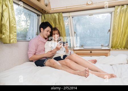 Jeune couple utilisant un smartphone sur le lit d'un camping-car van motorhome Banque D'Images