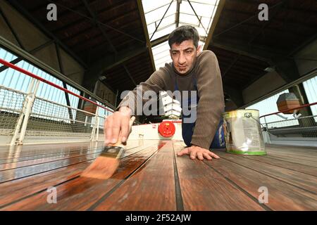 Friedrichshafen, Allemagne. 23 mars 2021. Abdulrahman Manos, employé de la Lake Constance Shipping Company (BSB), brosse la terrasse en bois du bateau à moteur Reichenau avec de l'huile de bois. Le bateau à moteur Reichenau est en préparation pour la saison dans le chantier naval de Friedrichshafen. (À dpa: 'Bateau d'excursion 'Reichenau' à embellir dans le chantier naval') Credit: Felix Kästle/dpa/Alay Live News Banque D'Images