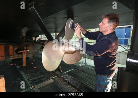 Friedrichshafen, Allemagne. 23 mars 2021. Eric Santos, employé du Bodensee Schiffsbetriebe (BSB), utilise une ponceuse orbitale pour meuler l'hélice du bateau à moteur Reichenau, qui est en préparation pour la saison au chantier naval de Friedrichshafen. (À dpa: 'Bateau d'excursion 'Reichenau' à faire dans le chantier naval') Credit: Felix Kästle/dpa/Alay Live News Banque D'Images