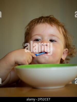 Portrait d'un enfant de race blanche mignon avec une cuillère. Bébé salissant avec une assiette. Banque D'Images
