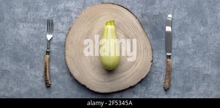 Courgette verte simple mûre fraîche sur la planche à découper avec fourchette et couteau sur fond gris table de cuisine. Banque D'Images