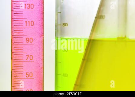 Macro photographie de l'eau rose, verte et jaune dans un bécher, une fiole et un cylindre gradué. Fond blanc. Banque D'Images