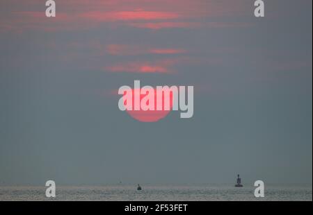 New Forest, Hampshire. 24 mars 2021. Météo Royaume-Uni. Le soleil se lève à travers la brume au-dessus du Solent, photographié de Lepe Beach dans la Nouvelle forêt. Credit Stuart Martin/Alamy Live News Banque D'Images