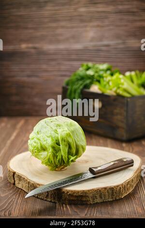 Laitue iceberg fraîche sur planche à découper en bois (mise au premier plan) Banque D'Images