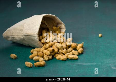 Arachide en noix qui est très sain, disposé dans un sac de toile de jute qui est renversé sur un fond texturé vert foncé. Banque D'Images