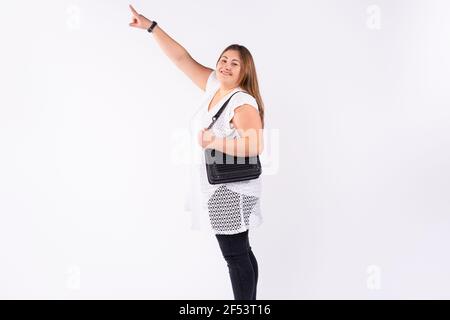 Une femme caucasienne de plus grande taille regarde la caméra avec un sourire et pointe son index vers le haut. Fond de studio blanc. Photo pleine longueur avec Banque D'Images