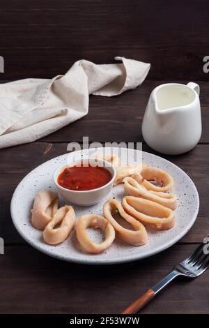 Rondelles de calmar frites avec sauce tomate et citron. Arrière-plan en bois foncé Banque D'Images