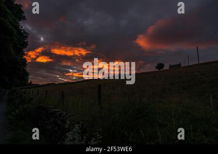 Des nuages orange spectaculaires au coucher du soleil derrière une maison isolée au sommet d'une colline à Weardale, dans le nord des Pennines, dans le comté de Durham, au Royaume-Uni Banque D'Images