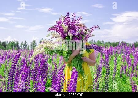 Femme blonde dans une robe jaune dans le champ lupin. Jour ensoleillé d'été. Concept détente, vacances, liberté. Banque D'Images