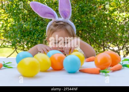 Mignon petit bébé habillé comme un lapin jouant avec de jolis œufs colorés. Décorations de Pâques traditionnelles. Vacances chrétiennes de printemps Banque D'Images