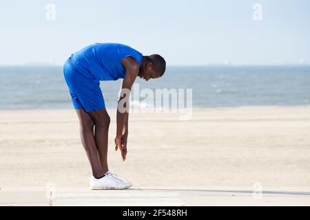 Portrait du corps entier sur le côté de la forme jeune homme s'exerçant sur la plage Banque D'Images