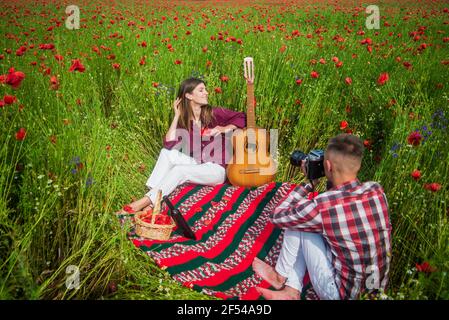 couple amoureux de faire des photos sur caméra avec guitare acoustique dans le champ de fleurs de pavot d'été, temps libre. Banque D'Images