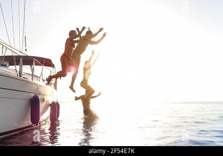 Vue latérale des jeunes amis du millénaire qui sautent du voilier Voyage sur l'océan - les garçons et les filles s'amusent l'été ensemble le jour de la fête en bateau à voile
