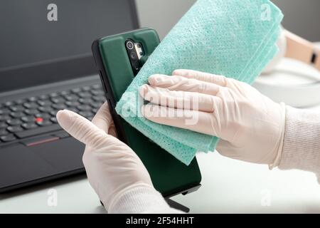 Femme en gants essuie le phomellapse avec le tissu humide et le désinfectant pendant le Covid 19. Désinfection phomeand ordinateur portable clavier par alcool désinfectant par Banque D'Images