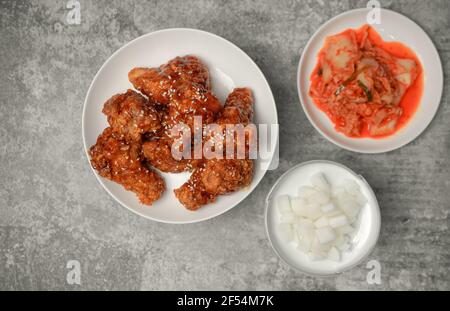 Vue de dessus poulet coréen épicé au friture surmontée de sésame blanc avec des kimchi et des plats d'accompagnement de radis marinés sur la table en béton gris, populaire pouo de rue Banque D'Images