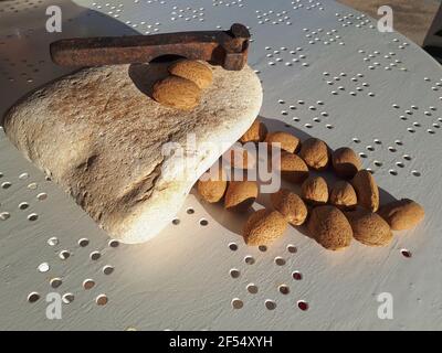 Tas d'amandes fraîches, pierre plate et un marteau rouillé pour écraser les noix sur la table Banque D'Images