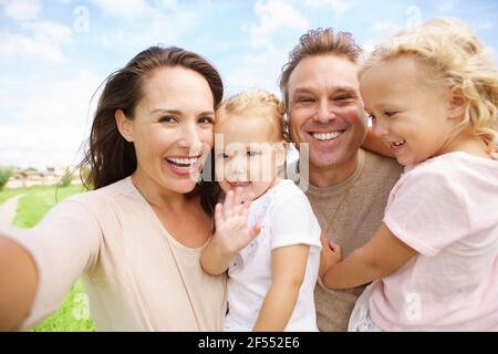 Portrait de famille heureuse avec deux filles prenant le selfie à l'extérieur Banque D'Images