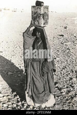 Ghat, Libye. Tuaregfrau (Targia) en vêtements folkloriques typiques avec réservoir de benzine comme réservoir d'eau, portant sur la tête Banque D'Images
