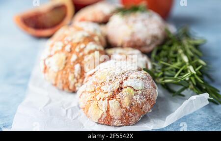 Petits gâteaux faits maison à l'orange avec sucre en poudre sur papier à pâtisserie, fond en béton bleu. Biscuits aux agrumes fissurés. Mise au point sélective. Banque D'Images